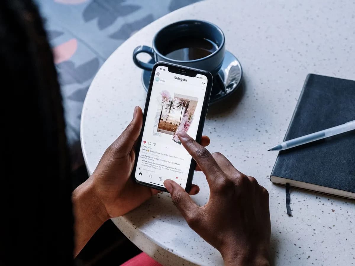 Manos sosteniendo un celular junto a una taza de café y una libreta sobre una mesa
