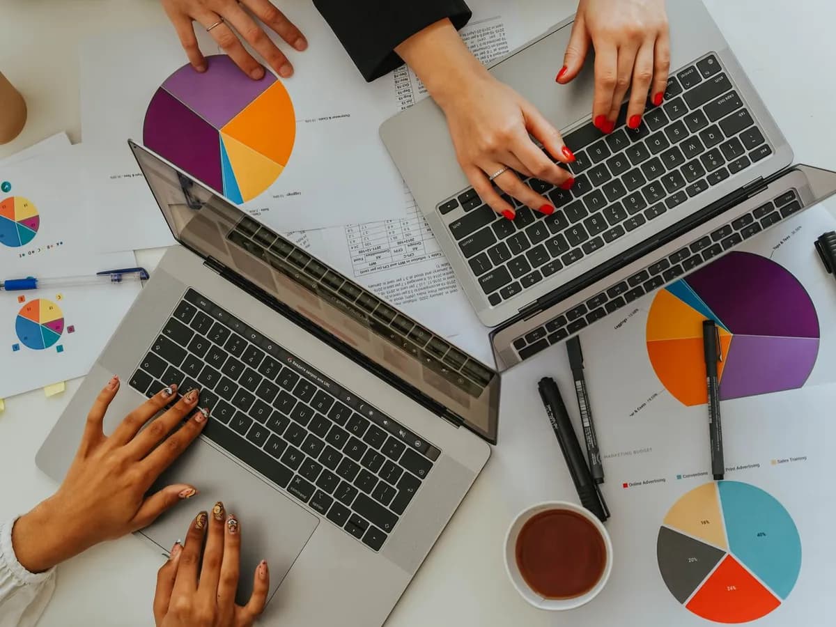 Personas trabajando con laptops sobre una mesa con gráficos y datos impresos